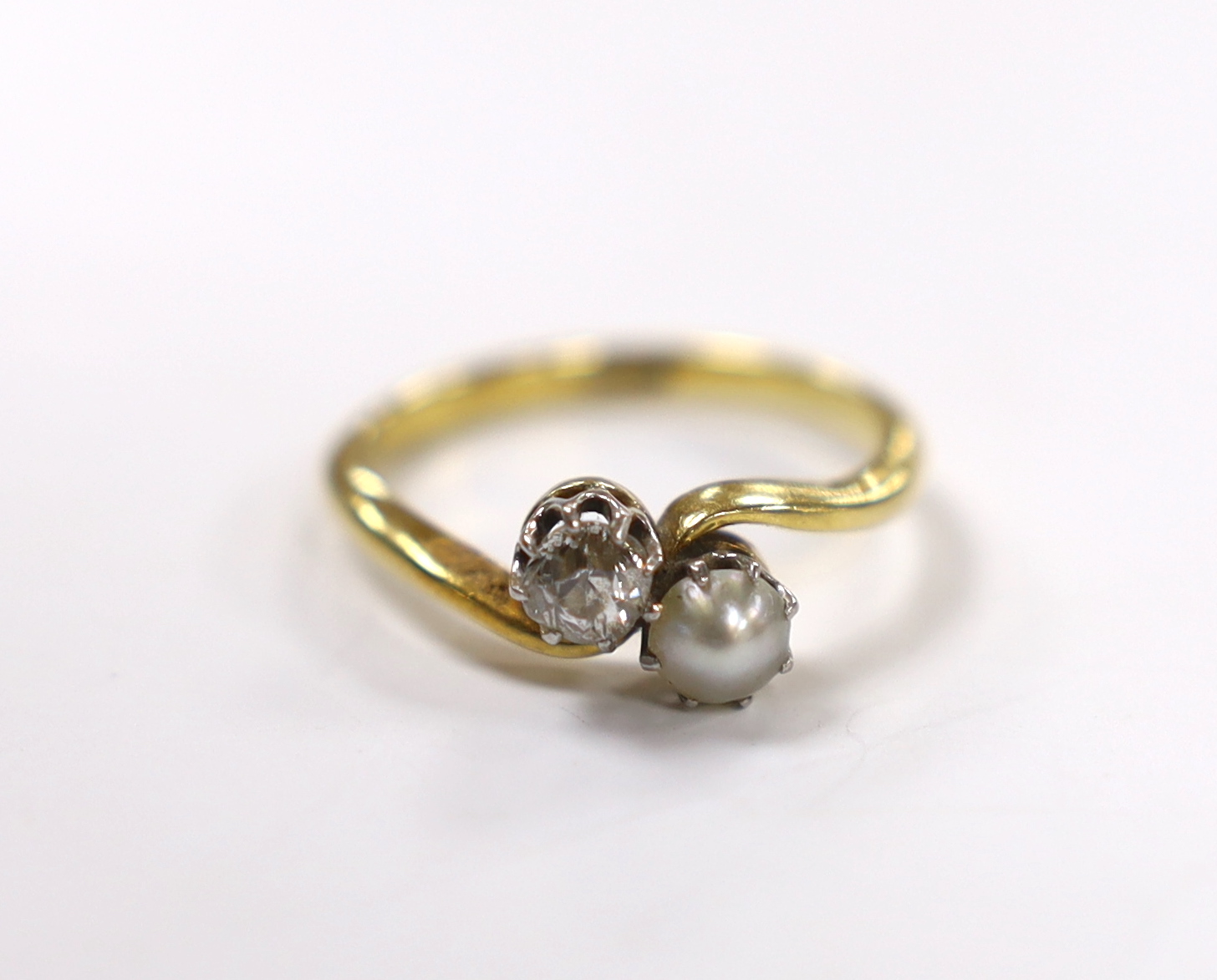 An 18ct, single stone diamond and single stone cultured pearl set crossover ring, size L/M, gross weight 2.6 grams.